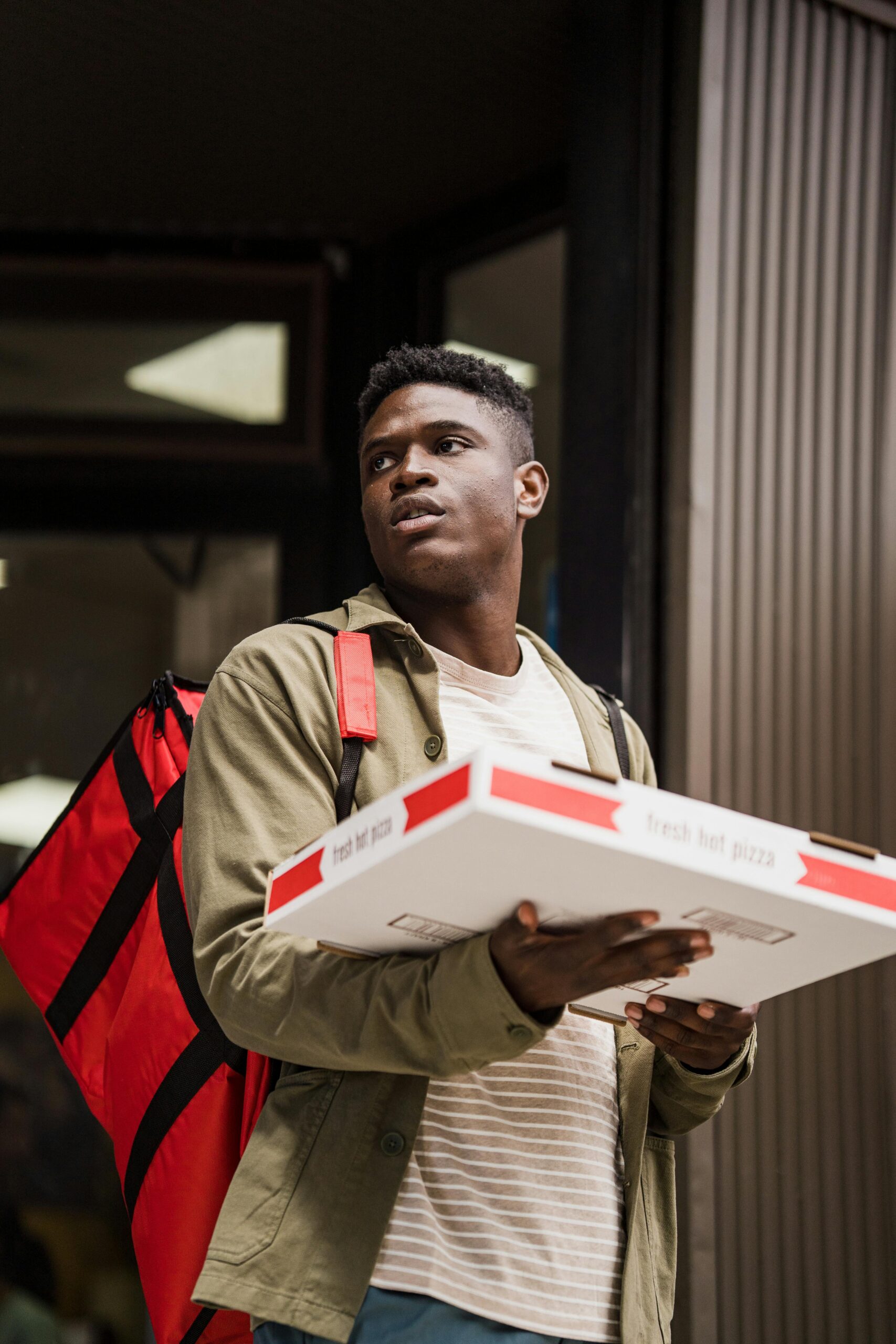 A delivery person holds pizza boxes outdoors with a red backpack, ready for delivery.