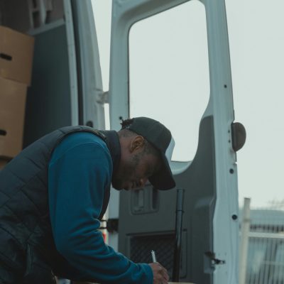 pexels-photo-6169191-6169191 A delivery worker signs documents outside a parked van, managing logistics efficiently.